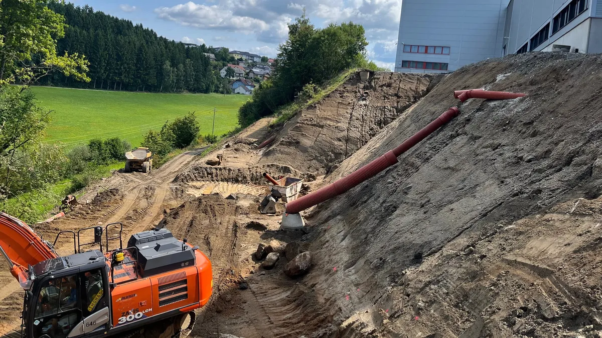 Steile Stützkonstruktion aus bewehrter Erde neben der neuen Halle
